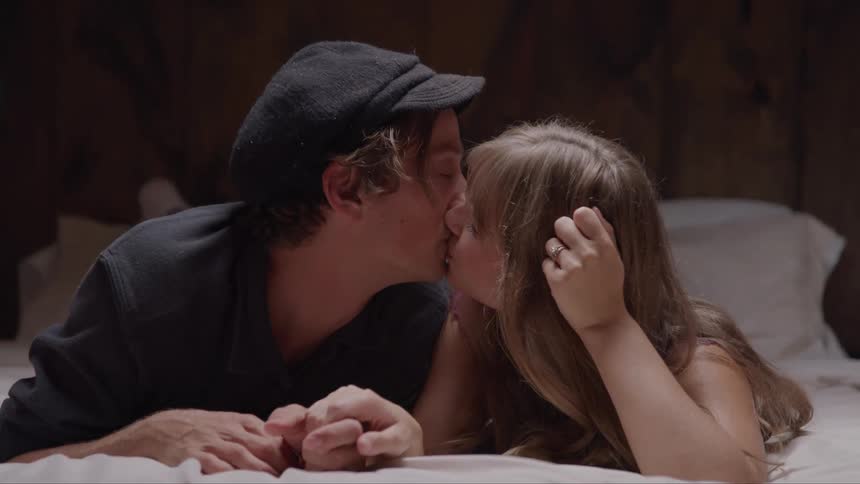 A man and a woman lay on a bed look at each other and share a kiss