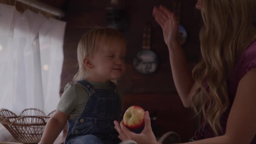A mother lovingly feeds an apple to her young son indoors