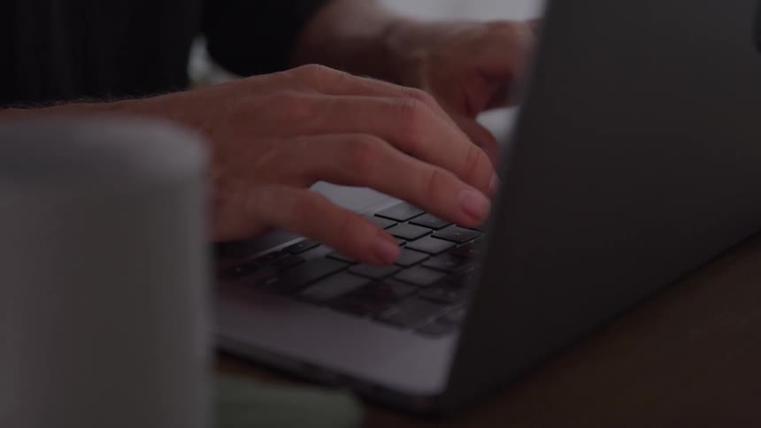 A persons hands type on a laptop keyboard