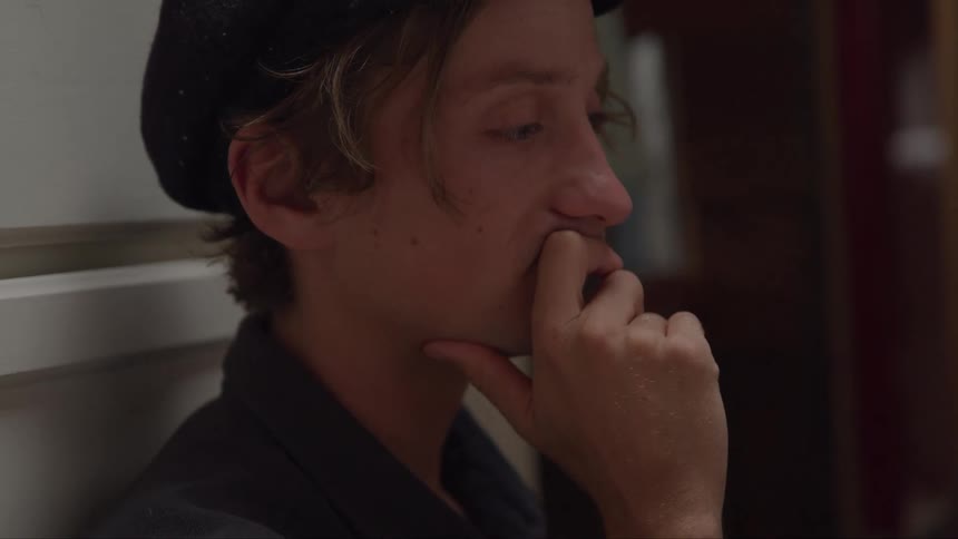 A person with a hat sits with a hand on their chin