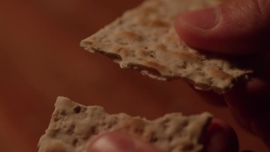 A person holds a thin cracker in their hands and snaps it in half