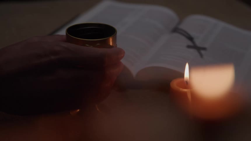 Closeup of a chalice beside a candle and open scripture during quiet devotion