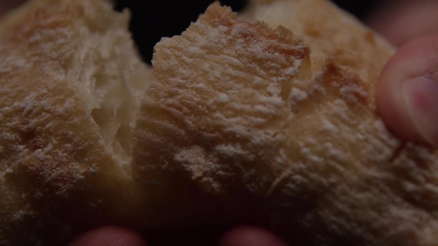 A pair of hands holds and breaks open a piece of crusty bread