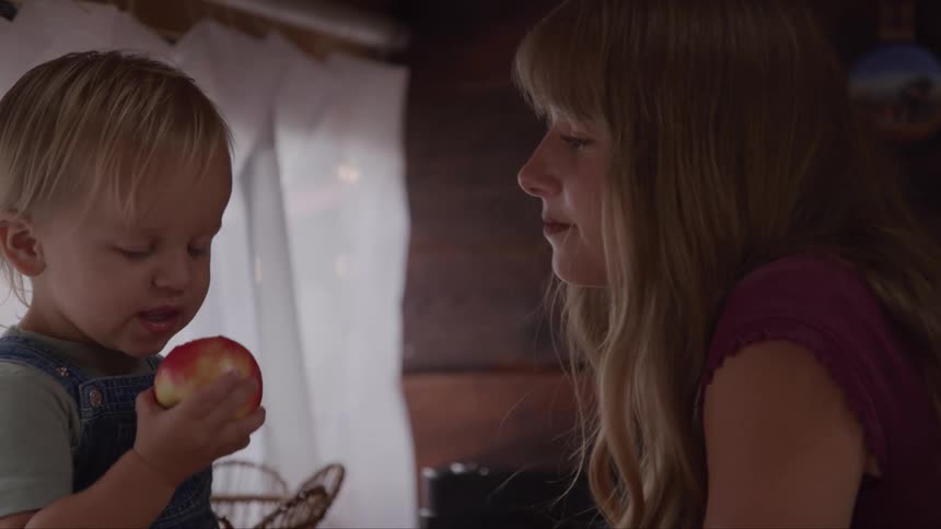 The video shows a young woman with a long blonde ponytail holding a small child with short blonde hair the woman is smiling and looking down at the child