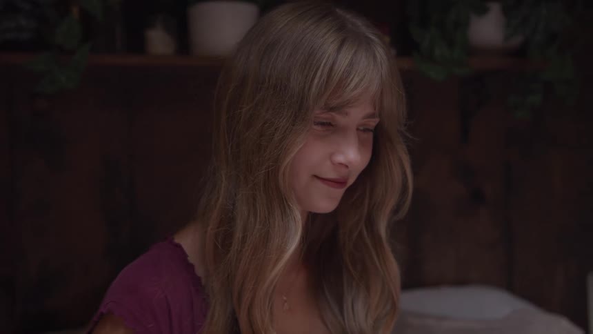 A young woman sitting on a bed smiles as she closes her laptop