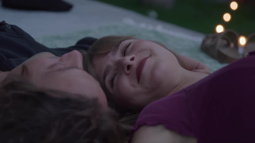 Couple relaxes on a blanket outdoors smiling beneath soft evening lights