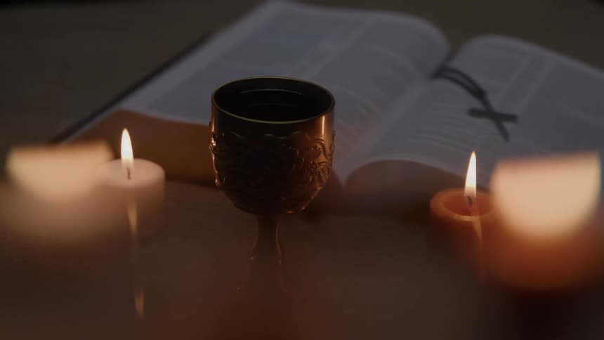 A chalice sits between candles beside an open book