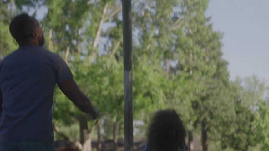 A kid plays basketball in a park along with an adult by side