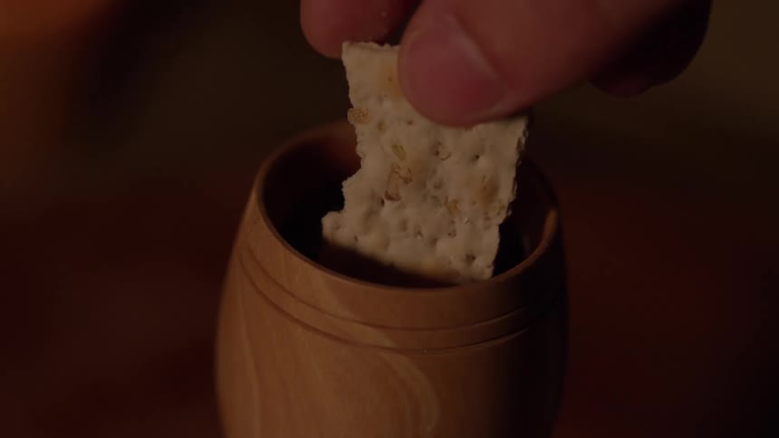 A hand dips bread into a wooden cup during a quiet moment