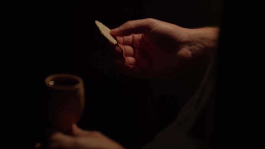 Hand holds a communion wafer while the other holds a wooden chalice