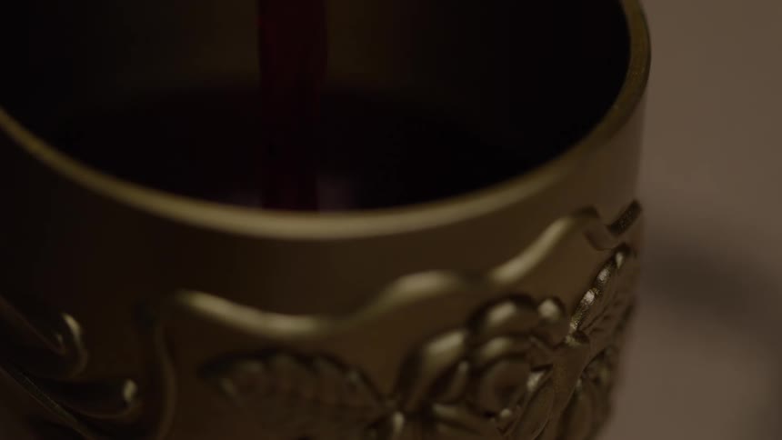 A dark colored liquid is poured into cup with a floral design on it