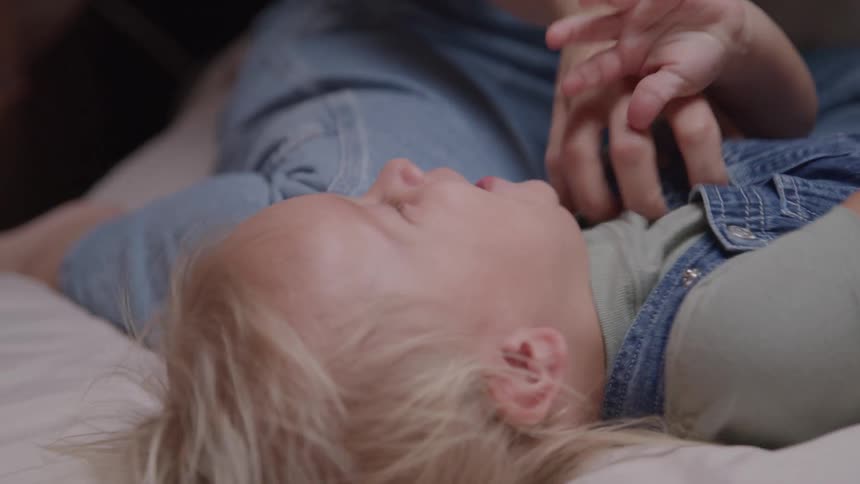 Mother tickles her male toddler as he is lying down on the floor indoors