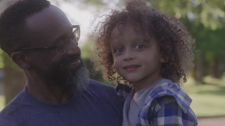 A father smiles while holding his young son outdoors