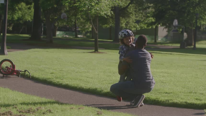 A boy drop his bicycle and go running to hug his dad in an outdoor setting