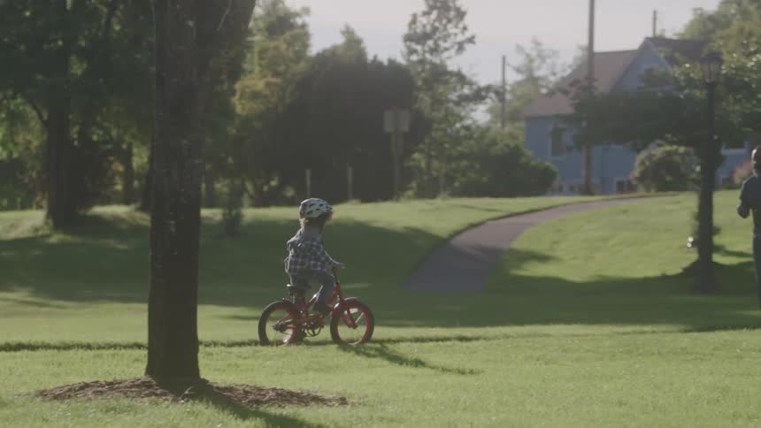 A girl on a bicycle rides in a grassy area in a park while other children play