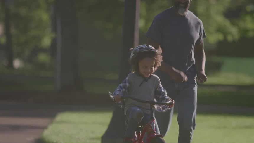 Young boy learing to ride a bike as his father jogs along at a park