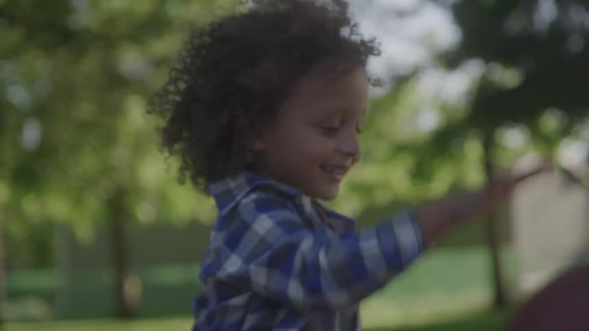 A child plays with a basketball in a grassy area with trees