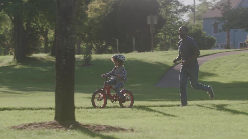 Father teaches his child how to ride a bicycle outdoors in a play area during daytime