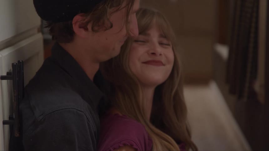 A young man hugs a young woman as they sit together on the floor