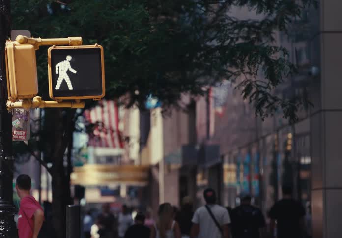 On a bustling city street a pedestrian crosswalk signal changes from the white walk icon to a flashing red hand indicating to stop