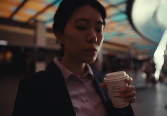 Woman views her smartphone while standing in the central area of a mall near an escalator