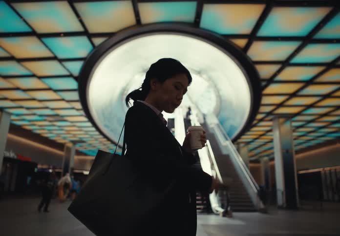 Woman taking a sip and using her smartphone heads to centrally located escalators