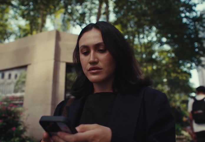 A woman pauses at the entrance to bryant park in new york city looks up thoughtfully and then checks her phone before walking out of the frame