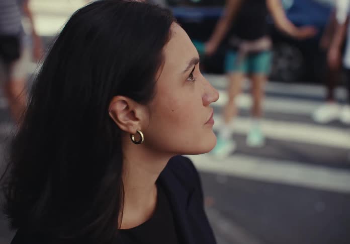 Female pedestrian waiting at an intersection looks around before crossing during the daytime