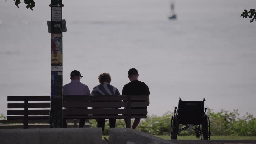 Two people sit together on a bench facing the water while a cyclist passes by in the foreground