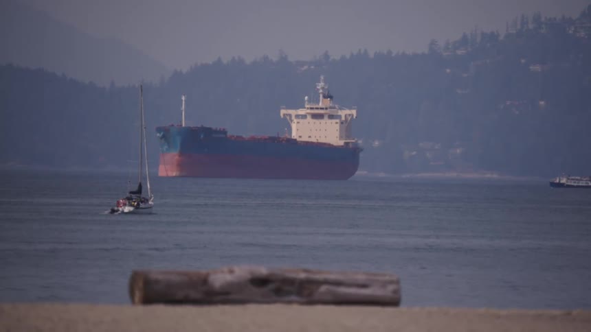 Cargo ship and sailboat sail near the coast with mountains in the background