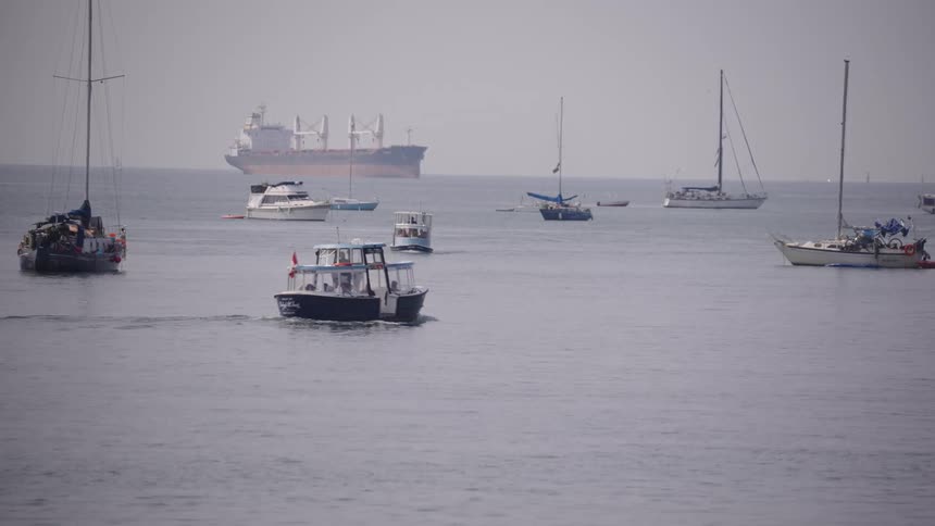 Motor powered watercraft travels past floating yachts while a ship sits on the horizon on a foggy day