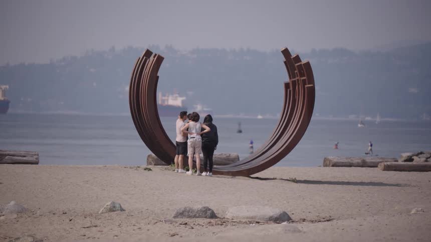 A group of people standing on a beach looking at a metal sculpture of multiple incomplete circles