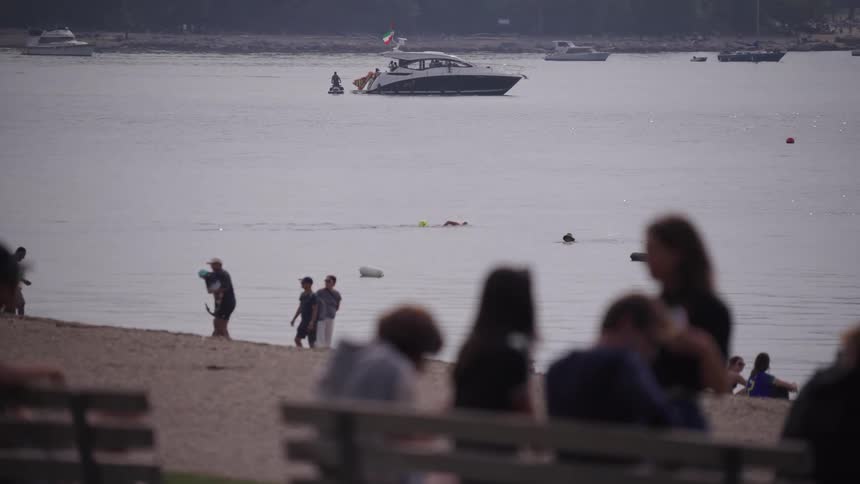 People walk on the sand while boats are anchored in the sea in the background