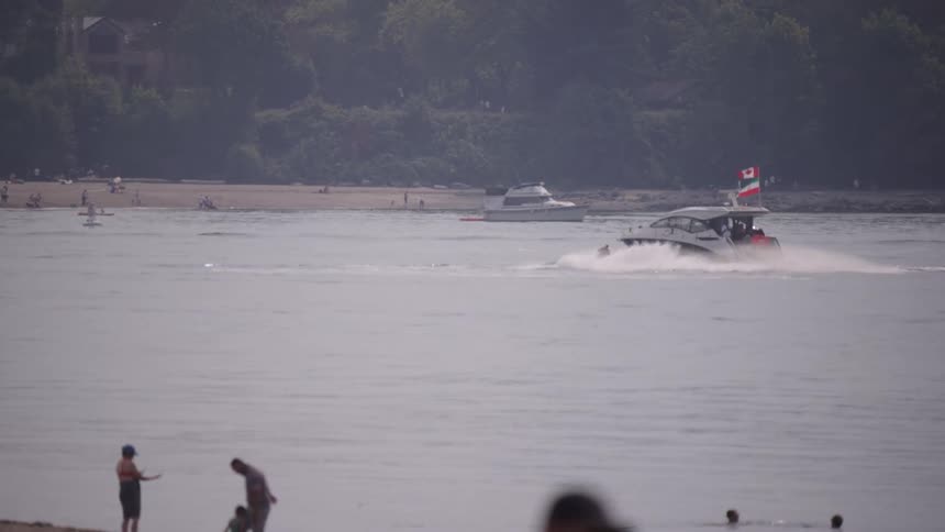 A body of water with a boat and people on a jet ski and a shore with people and trees in the background