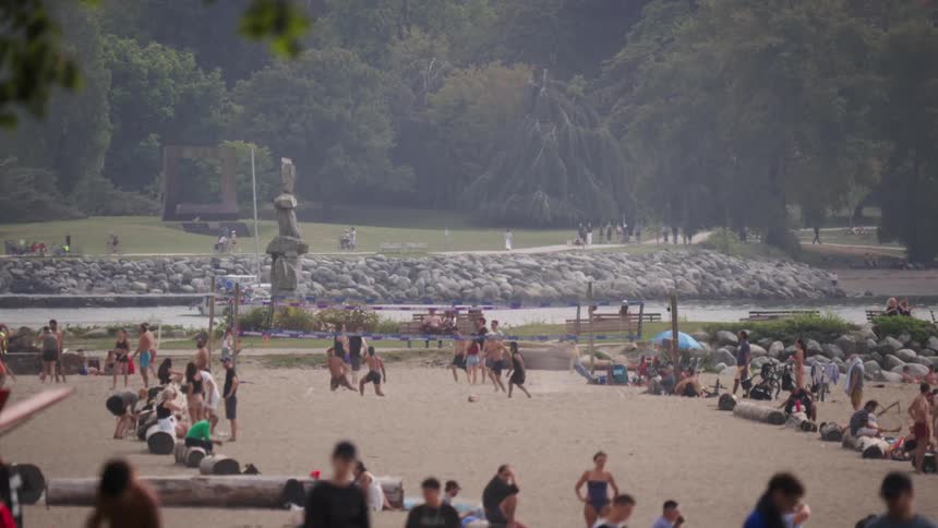 Group of people play beach volleyball while others relax on the sand near the monument