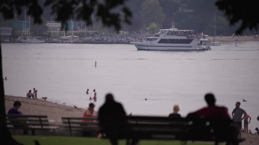 The video shows a busy beach scene on a hazy day in the background a motorboat is seen speeding across the water