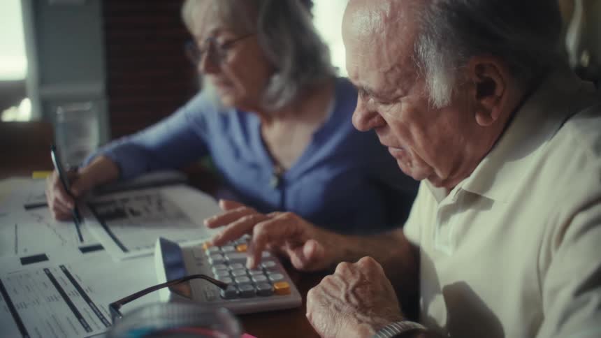 Elderly couple reviews documents while the man uses a calculator