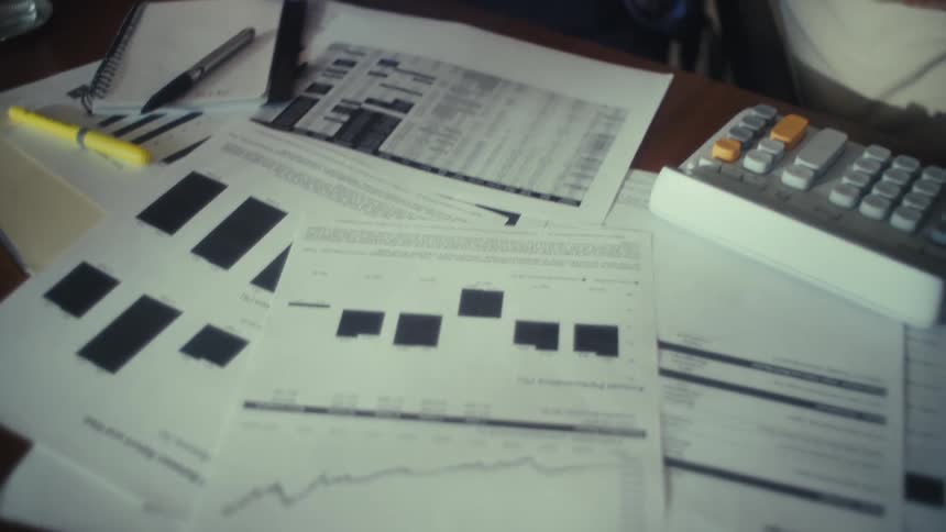 An elderly couple sits behind a desk covered with documents looking overly excited with each other at midday