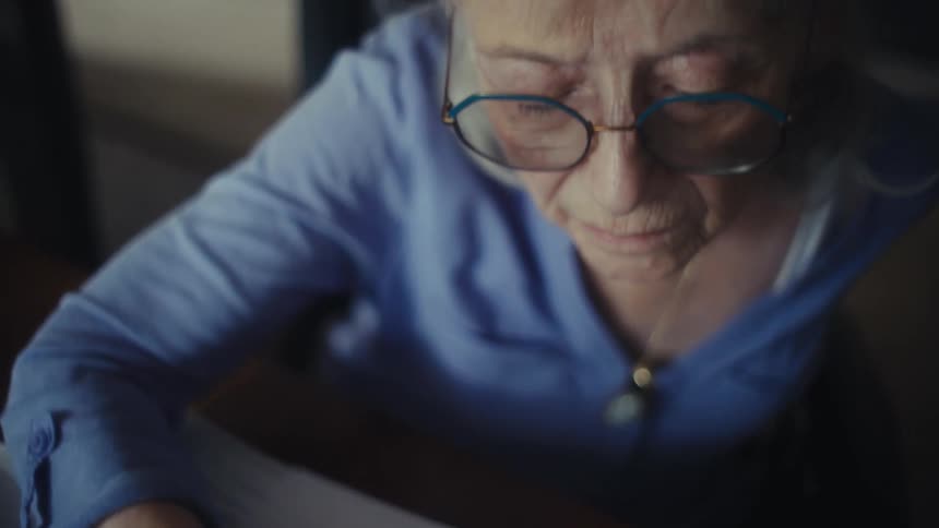 Elderly woman reviews printed spreadsheets with charts and notes while pointing at data with a pen