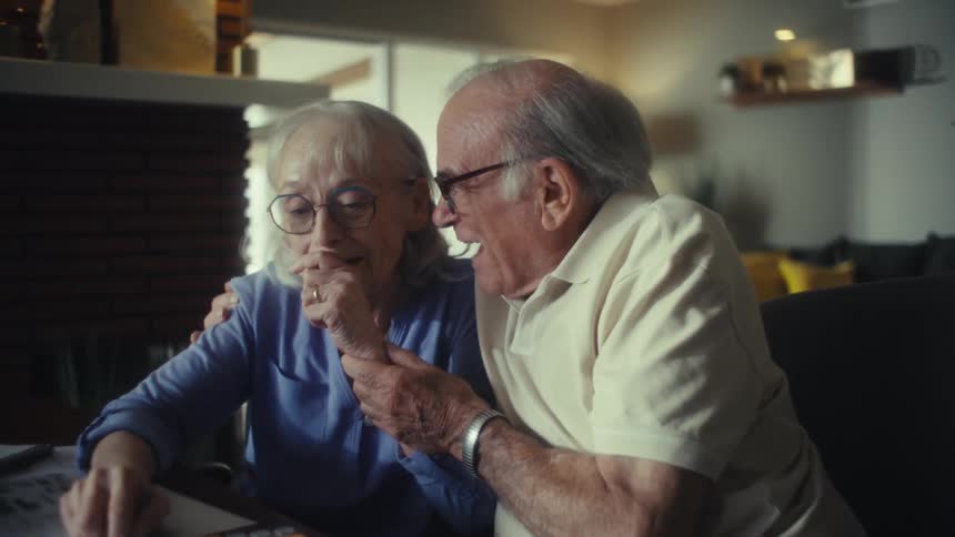 Elderly man smiles while hugging a thoughtful elderly woman beside him