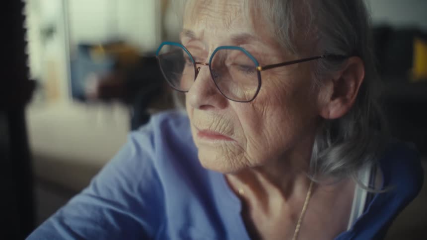 Screen reflects on the eyeglasses of a woman sitting in front of a computer at home