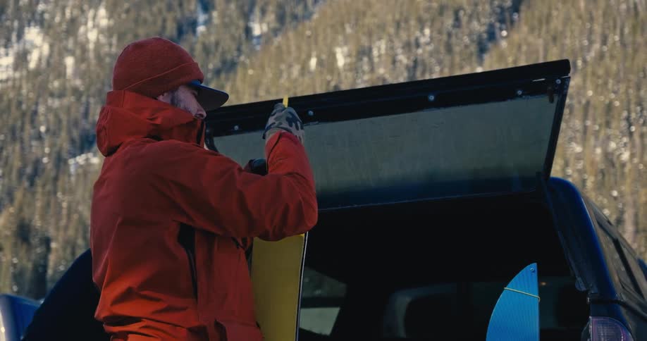 A person stands by a truck and puts a ski into the back of the truck