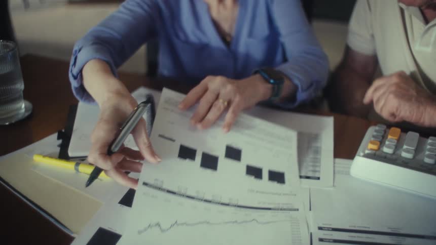 Elderly couple references financial information while sitting at their dining table at home