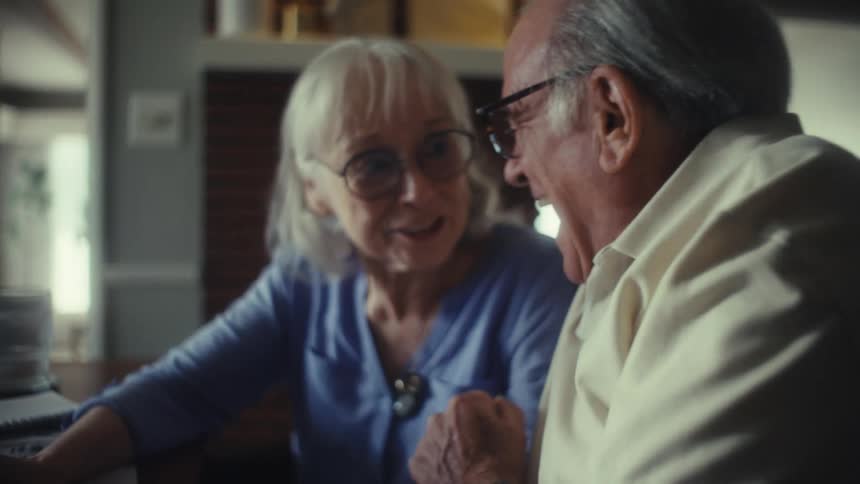 Elderly couple smiles and shares a look of complicity while talking at the table