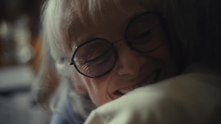 A beautiful elderly woman with white hair and glasses smiles joyfully she is laughing and interacting with someone out of frame