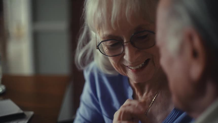 Elderly woman with glasses smiles while looking at the man beside her