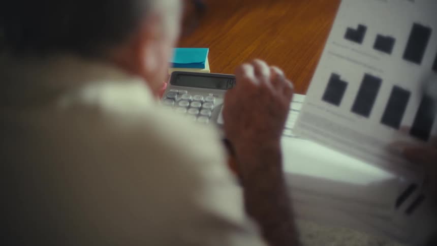 A man is typing numbers into a calculator while a woman holds paperwork