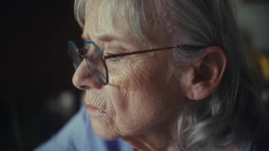 The video shows a closeup shot of an older woman with white hair and glasses she is looking intently at something out of frame