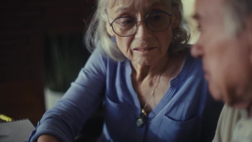 Elderly woman with glasses looks attentively at the man sitting beside her