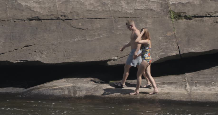A man and woman walk near the water holding hands